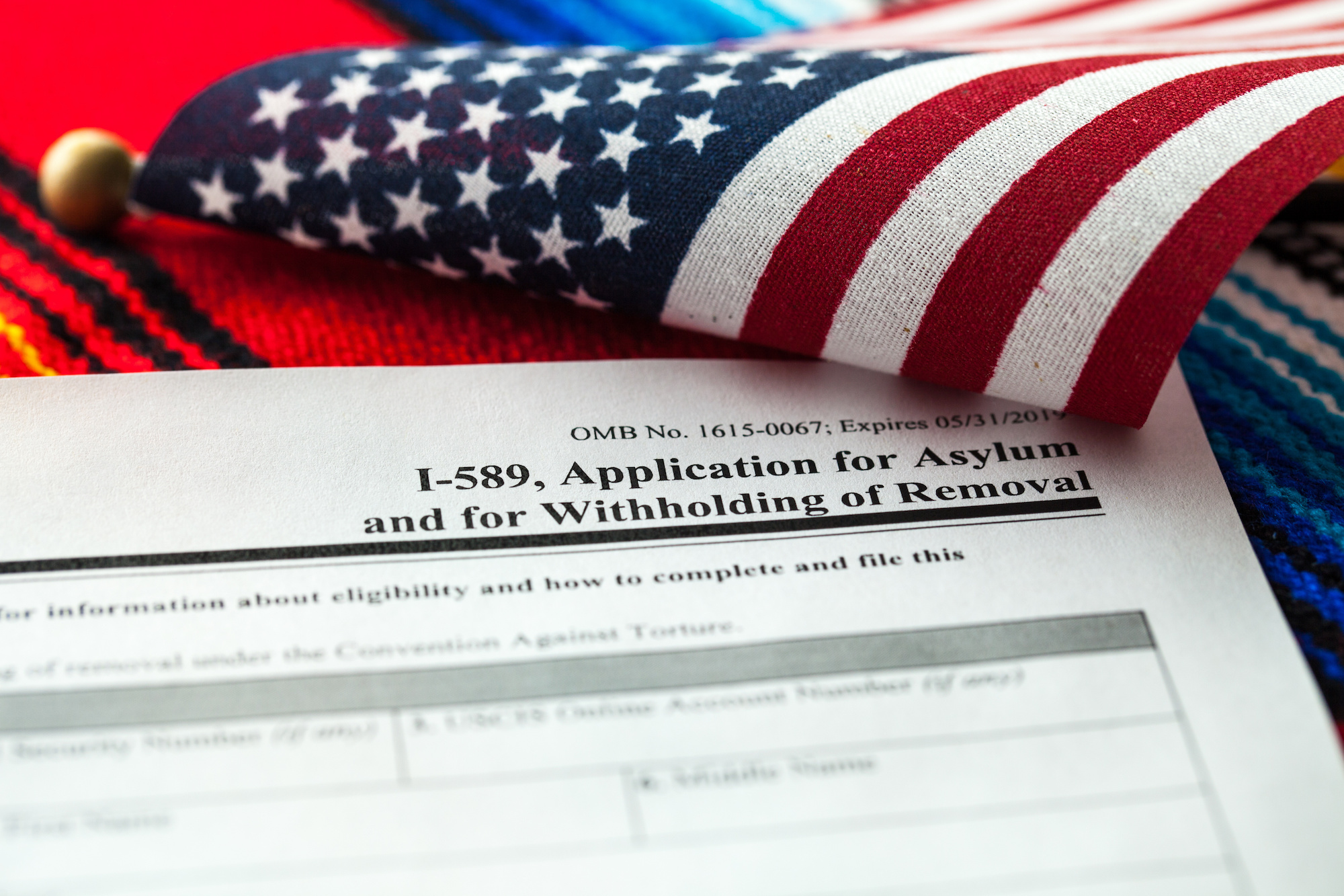 An Asylum application from the USICS next to a small American flag and over a sarape.